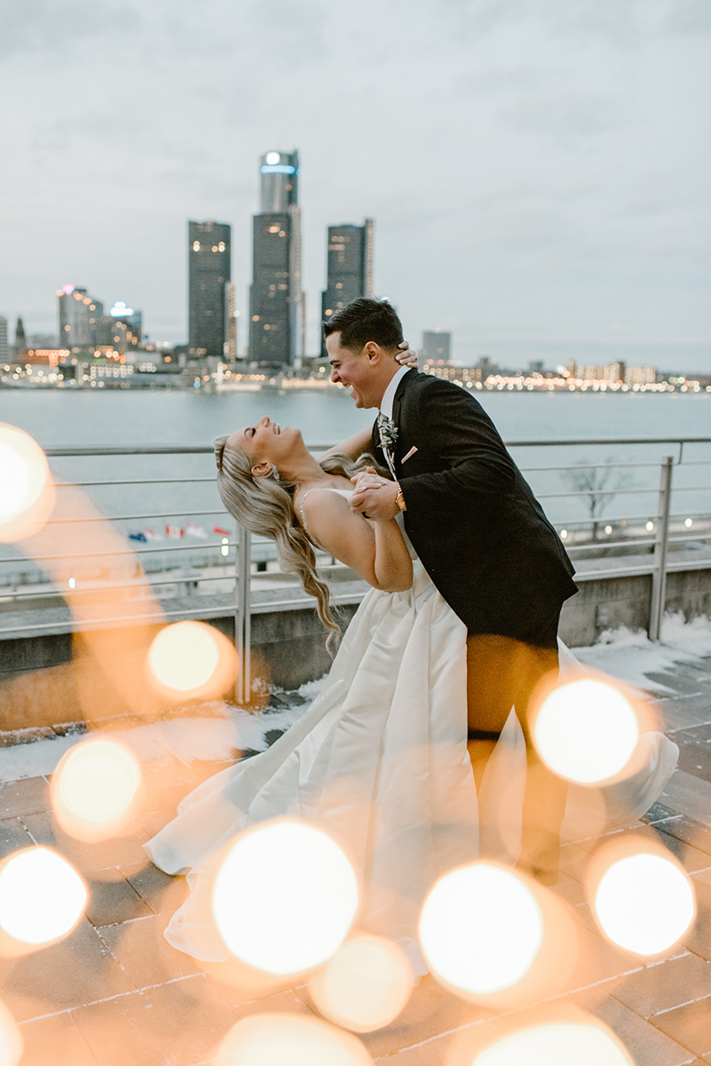 Bride and Groom laughing while dancing on rooftop overlooking Detroit skyline