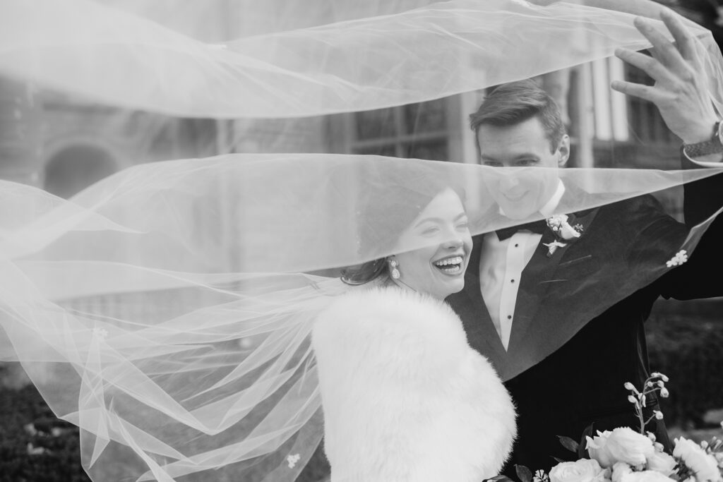 Candid moment with wedding couple and veil being swept with the wind.